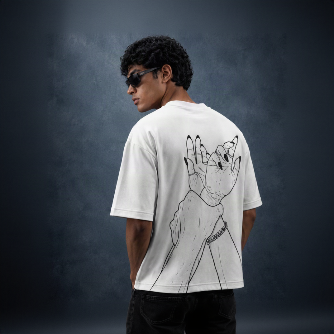 A man wearing a white t-shirt with a black line art graphic of a hand with long nails on the back, photographed from behind against a dark textured studio background.